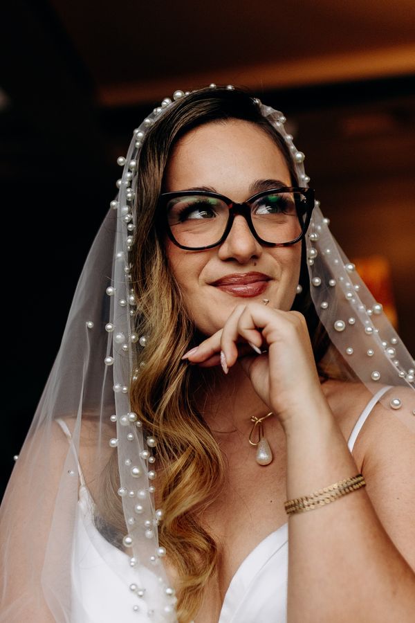 Novia con lentes y velo de perlas mirando hacia arriba
